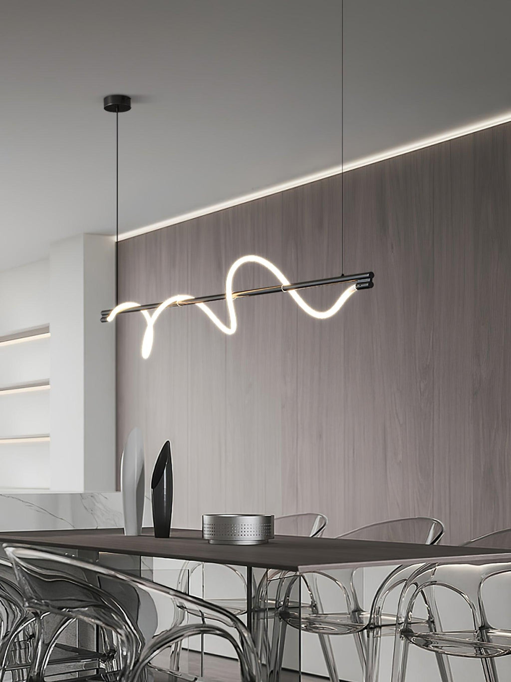 Black Clérachic linear pendant lit at an angle, with a wood wall, a cove light and acrylic chairs below.
