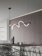 Black Clérachic linear pendant lit at an angle, with a wood wall, a cove light and acrylic chairs below.