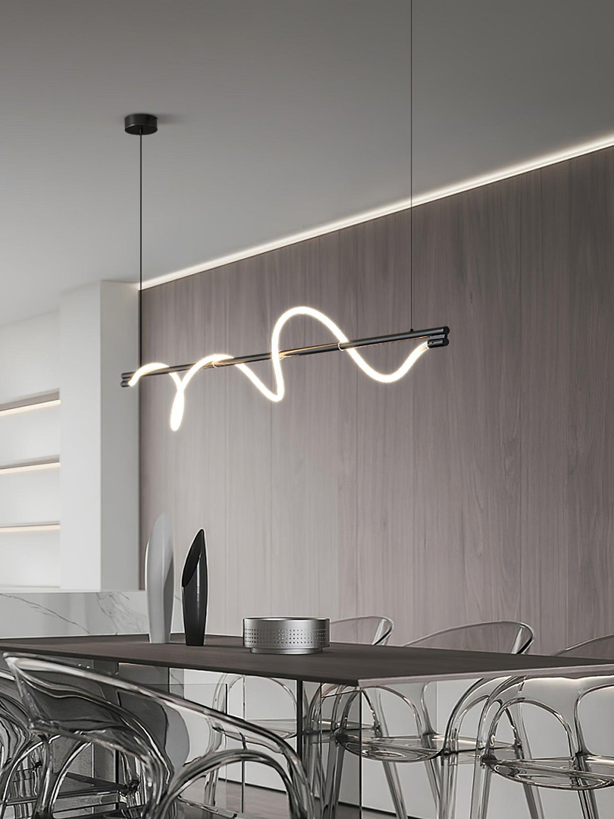 Black Clérachic linear pendant lit at an angle, with a wood wall, a cove light and acrylic chairs below.