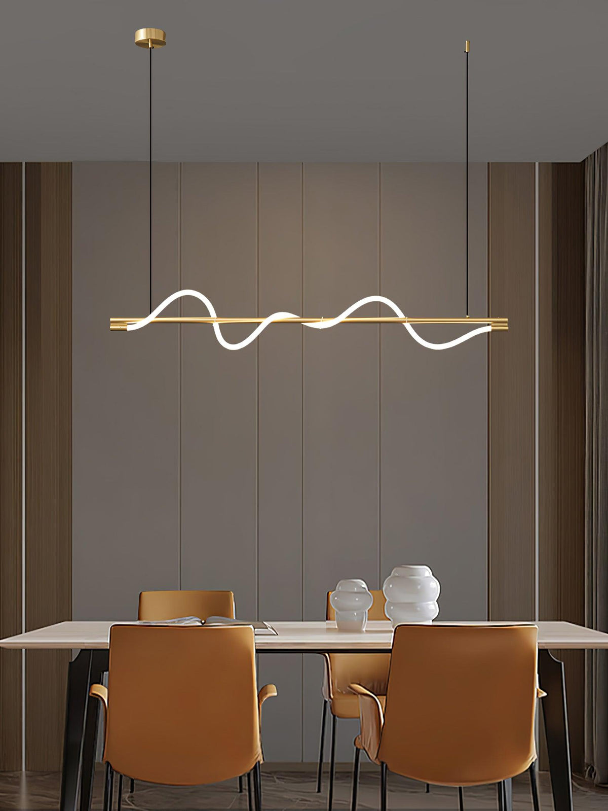 Brass Clérachic linear pendant above a table with rust leather chairs and two pale vases, against a taupe panelled wall.
