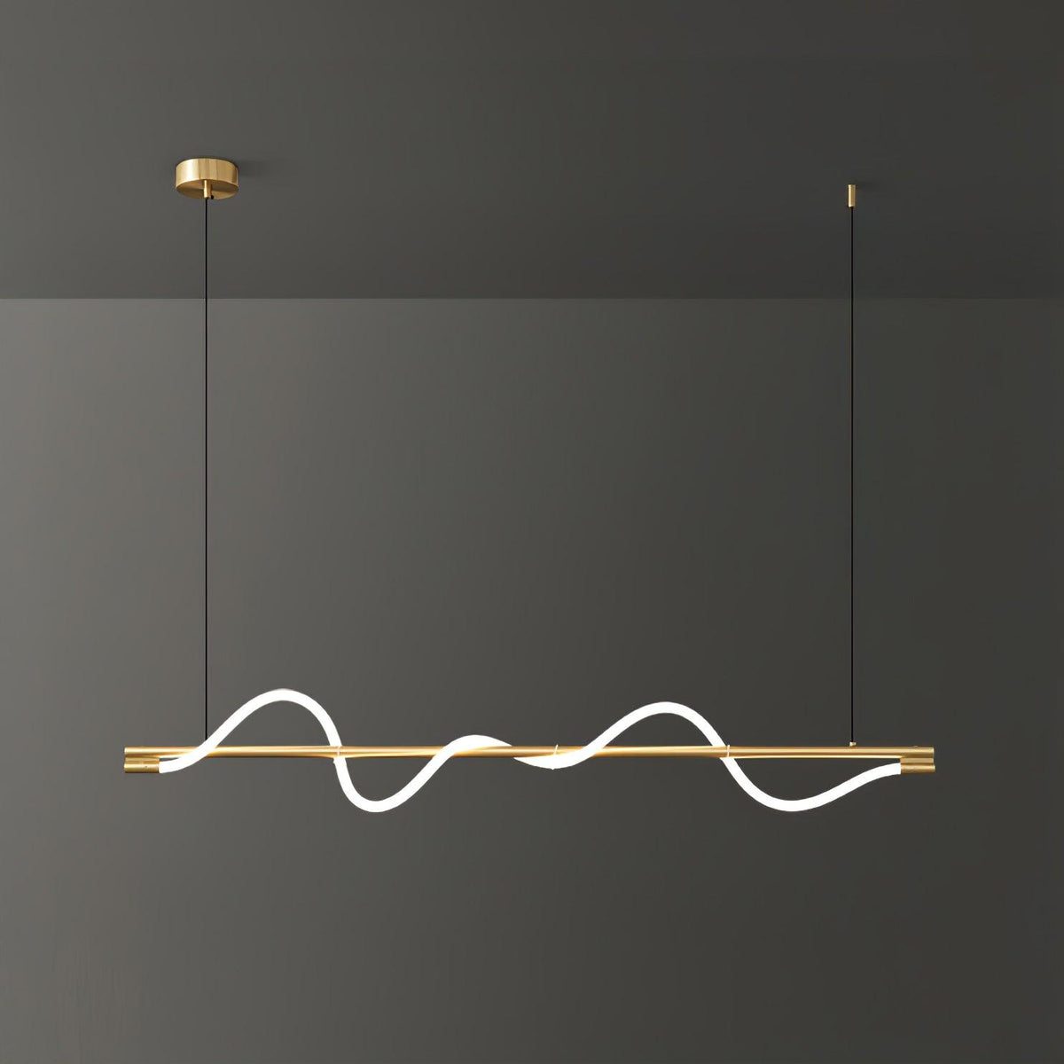 Brass Clérachic linear pendant with a bright wave, filling the frame against a dark grey wall.
