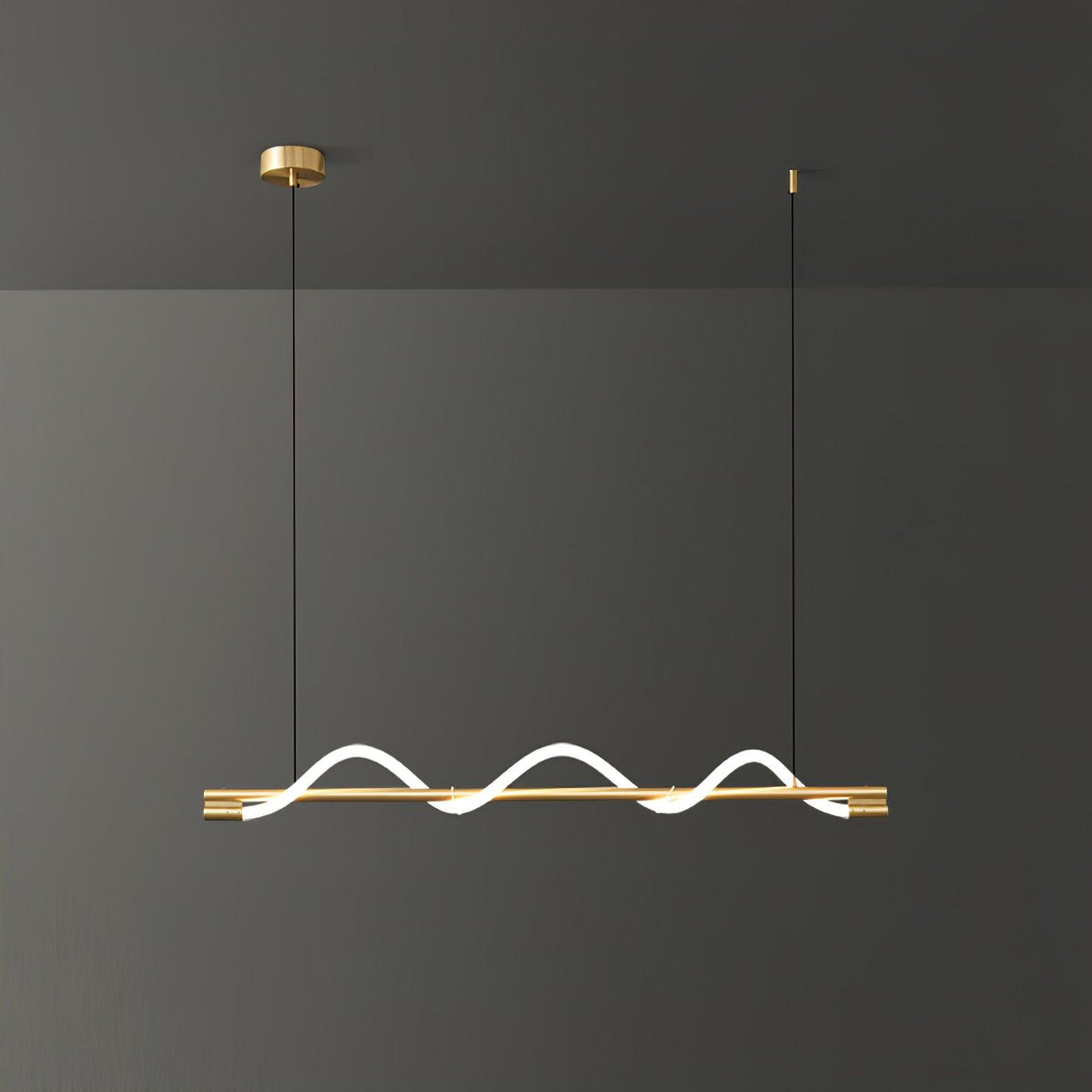 Brass Clérachic linear pendant with three tight glowing waves, against a dark grey wall.