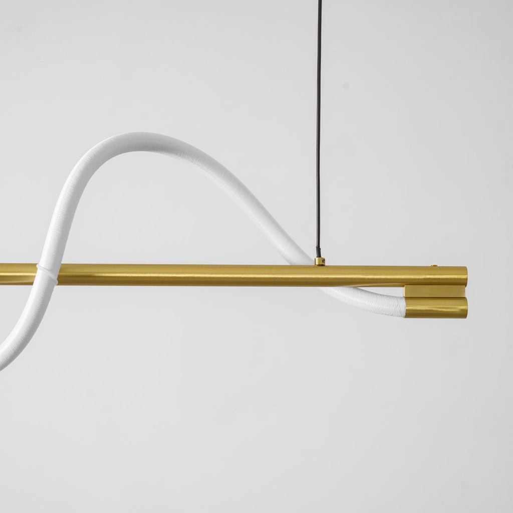 Close view of the white silicone line curving over the brass bar of this Clérachic linear pendant.