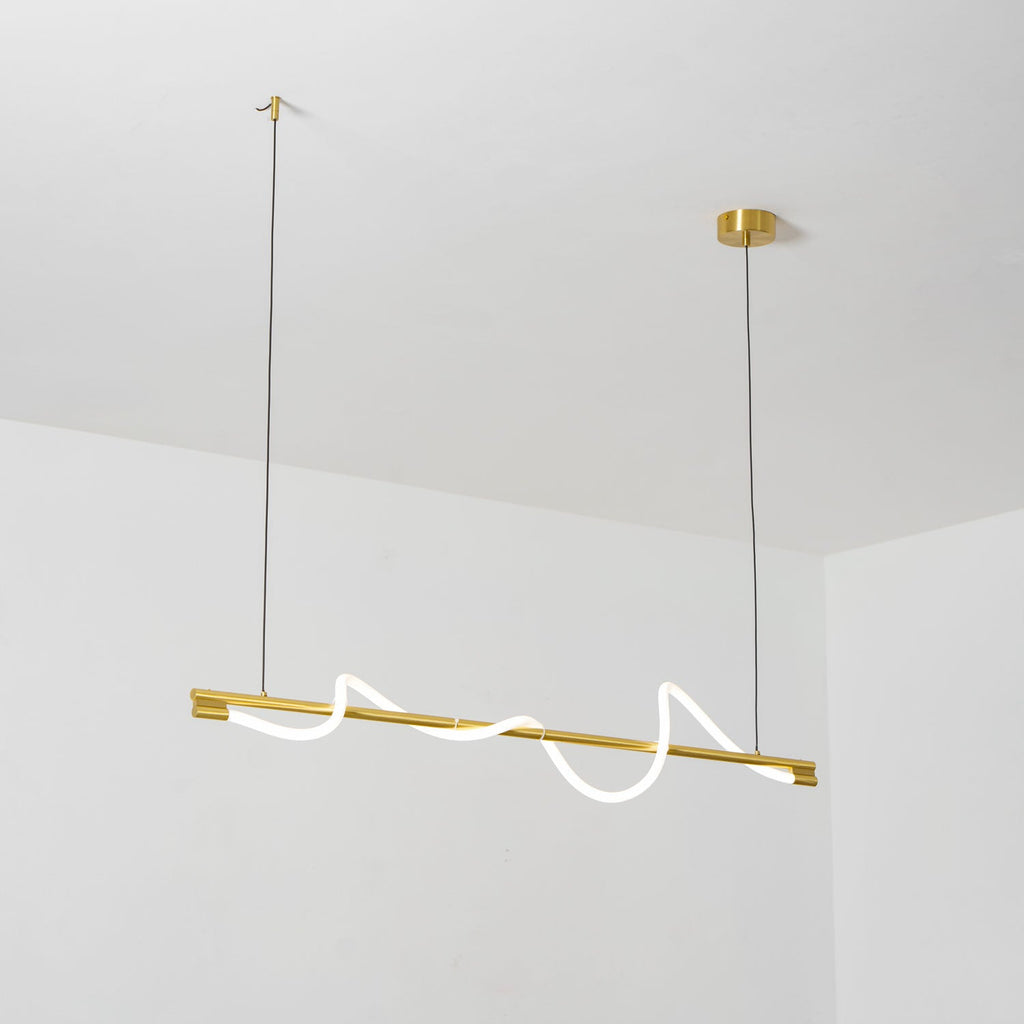 Looking up at a brass Clérachic linear pendant with a glowing wave, hung from a white ceiling.