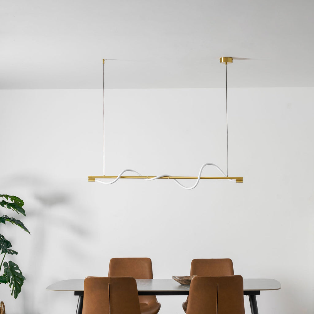 Clérachic brass linear pendant hung under a white ceiling, above a table with leather chairs and a green plant.