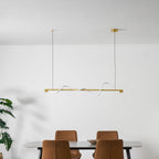 Clérachic brass linear pendant hung under a white ceiling, above a table with leather chairs and a green plant.