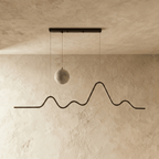 Clérachic 120 cm black pendant switched off, showing the grey moon-textured globe and the mountain-ridge metal line on limewash.