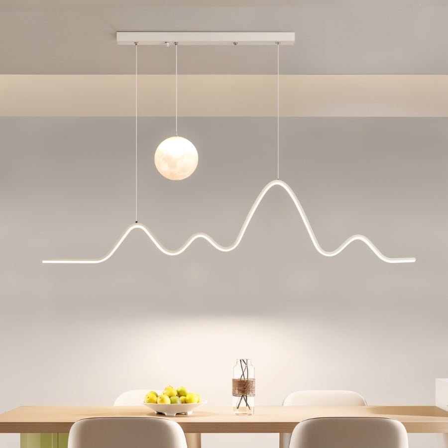 Clérachic 120 cm white pendant with a moon globe and mountain-ridge LED line hung above a pale wooden dining table with a fruit bowl.