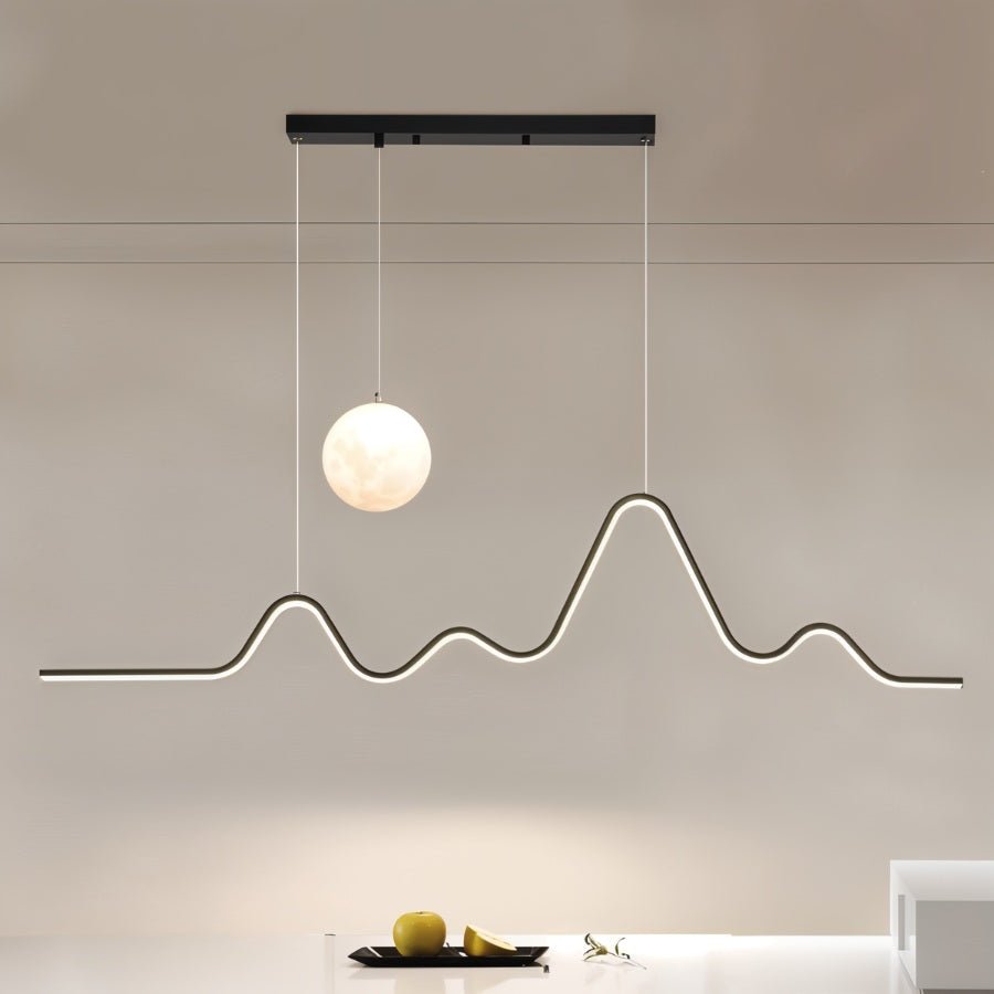 Clérachic 120 cm black pendant with a bright moon globe and a glowing LED line shaped like peaks, over a white counter and fruit.