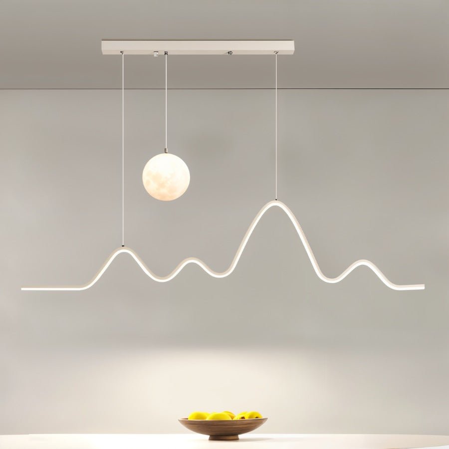 Clérachic 120 cm white pendant with a moon globe and a glowing peak-shaped LED line, hung above a table with a wooden fruit bowl.
