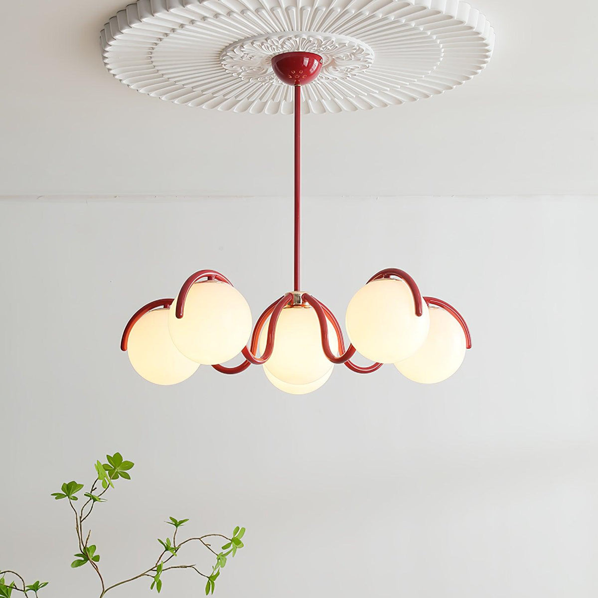Clérachic red-framed chandelier lit beneath a white ceiling rose, with six glass globes on wavy arms and a green sprig below.