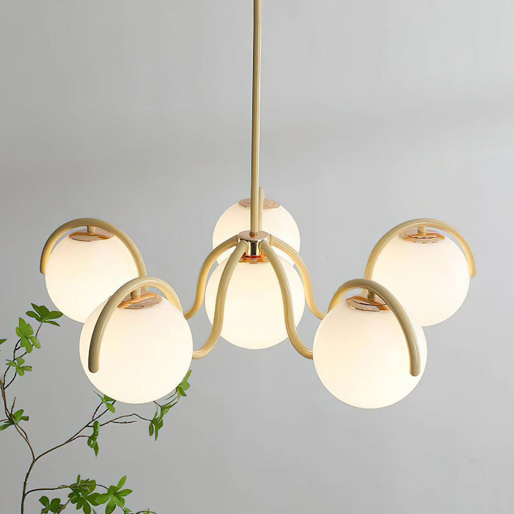 Close view of the creamy yellow arms and lit globes of this Clérachic chandelier, with leaves at the lower left.