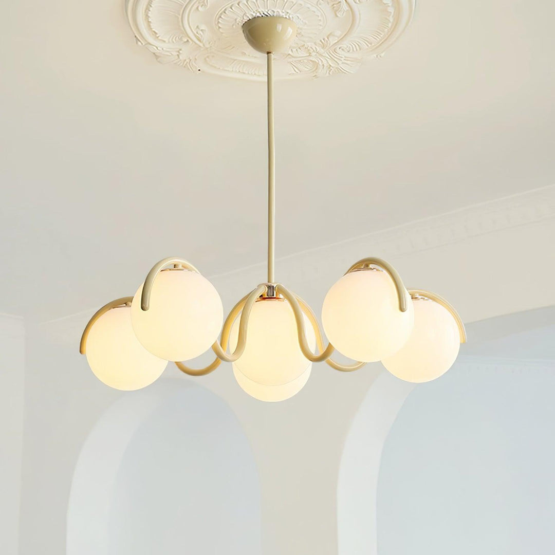 Clérachic creamy yellow chandelier lit in front of two white arched alcoves, below a plaster ceiling rose.