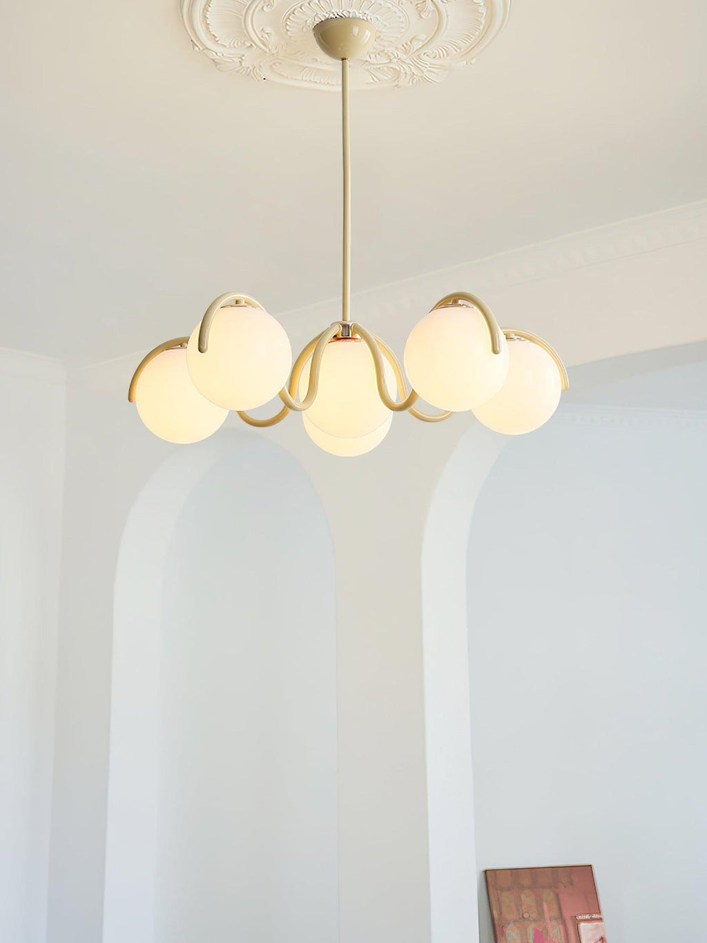 Creamy yellow Clérachic chandelier seen from a distance in a pale room, with arched alcoves and a book at the edge.