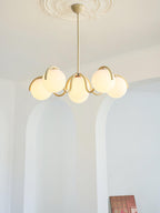Creamy yellow Clérachic chandelier seen from a distance in a pale room, with arched alcoves and a book at the edge.