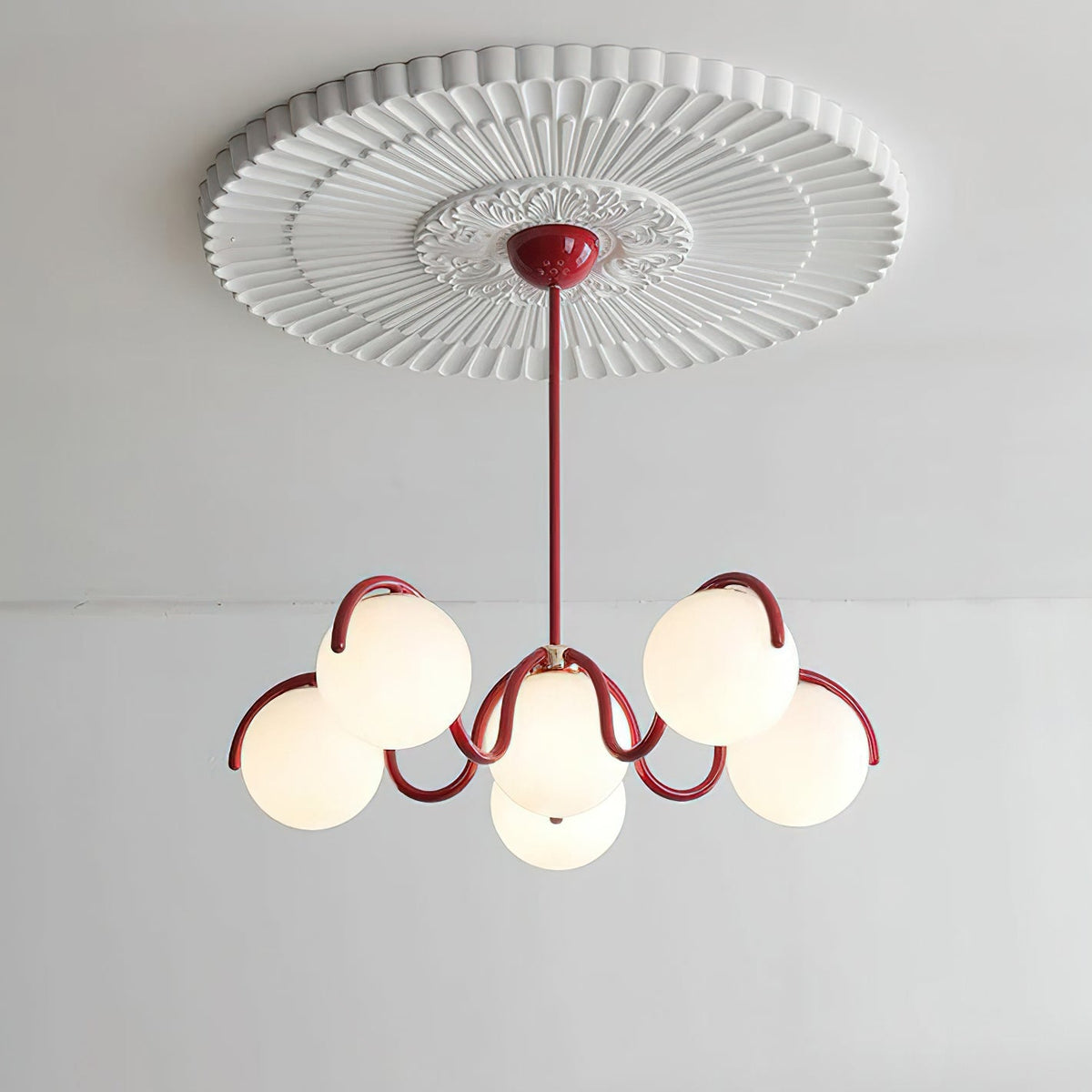A red Clérachic globe chandelier hung beneath a large white ceiling rose, its six globes lit.
