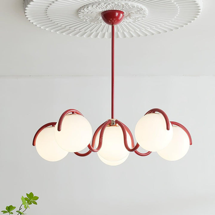 Red Clérachic chandelier under a white ceiling rose, with six glass globes lit and a green sprig at the lower right.