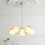 A creamy yellow Clérachic chandelier hung from a ceiling rose, with warm-lit globes and a sprig of leaves below.