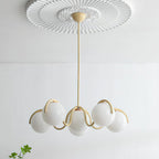 A creamy yellow Clérachic chandelier with its globes unlit, hung from a ceiling rose with a green sprig below.