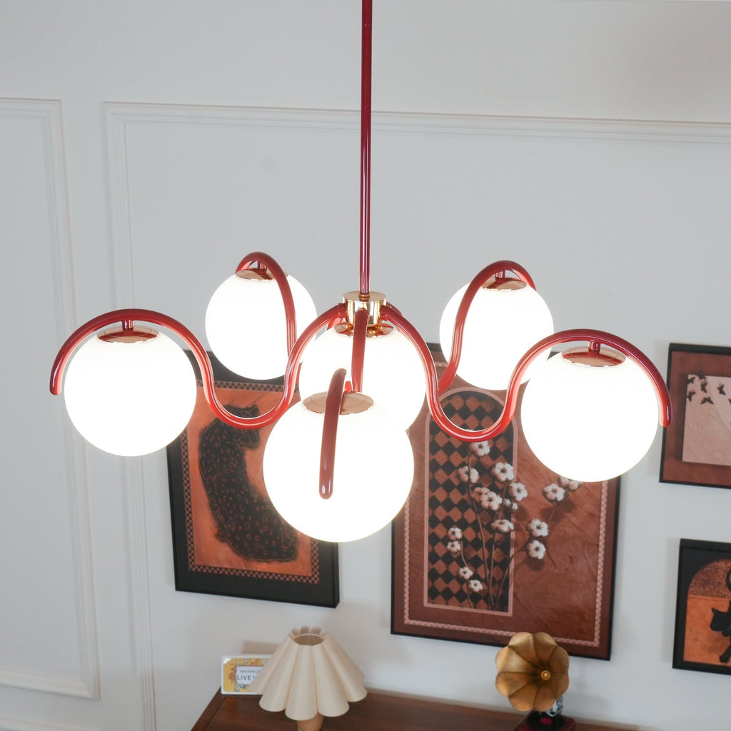 Red Clérachic chandelier lit above a dark wooden sideboard, with framed prints and a pleated lampshade behind.