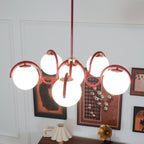 Red Clérachic chandelier lit above a dark wooden sideboard, with framed prints and a pleated lampshade behind.