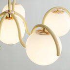 Close view of a creamy yellow arm and white glass globe on this Clérachic chandelier, with a brass-toned fitting at the top.