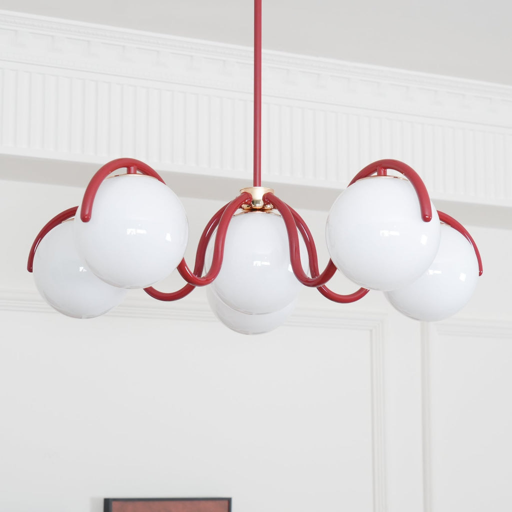 A red Clérachic chandelier seen from below against a white panelled wall, with a coved ceiling edge above.