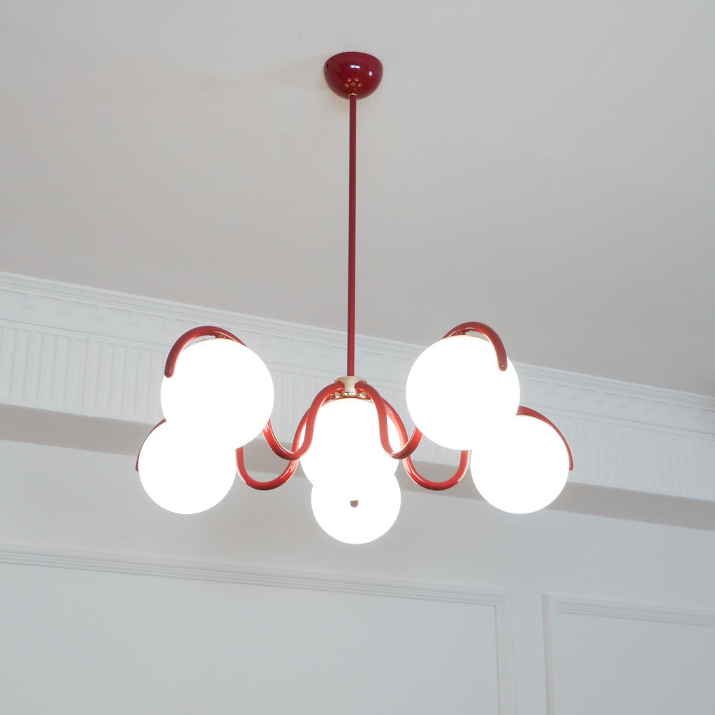 A red Clérachic chandelier from below with a round red canopy, its globes lit warm against a white cornice.