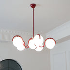 A lit red Clérachic chandelier seen from below, with its curving arms and globes in front of a white panelled wall.