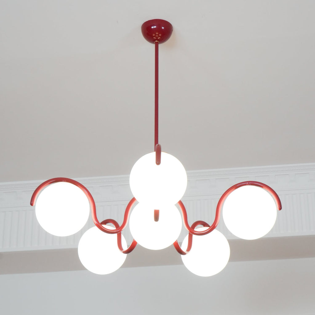 Looking up at this red Clérachic chandelier, its six lit globes arranged around the centre with a round red canopy above.