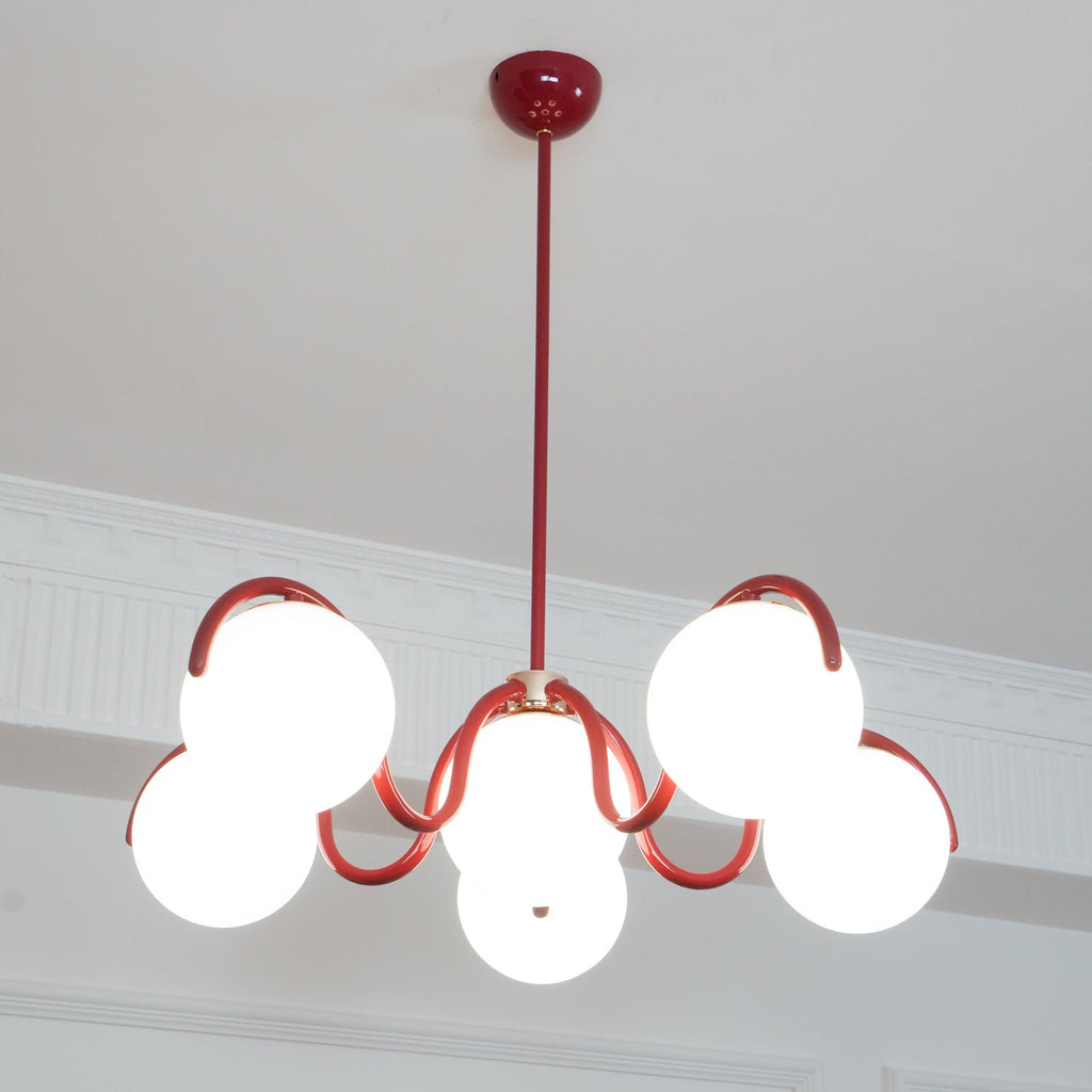 Lit red Clérachic chandelier seen from below, with its globes bright against a white panelled wall.