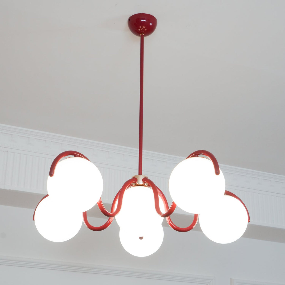 Lit red Clérachic chandelier seen from below, with its globes bright against a white panelled wall.