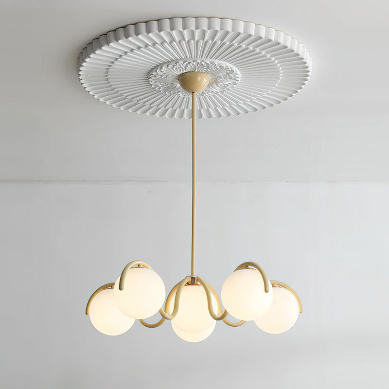 Creamy yellow Clérachic chandelier hung from a pleated ceiling rose, its six globes lit softly against a white wall.