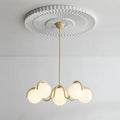 Creamy yellow Clérachic chandelier hung from a pleated ceiling rose, its six globes lit softly against a white wall.