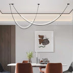 Clérachic pendant with two glowing LED curves above a marble-top table and rust-coloured chairs, a framed abstract print behind.