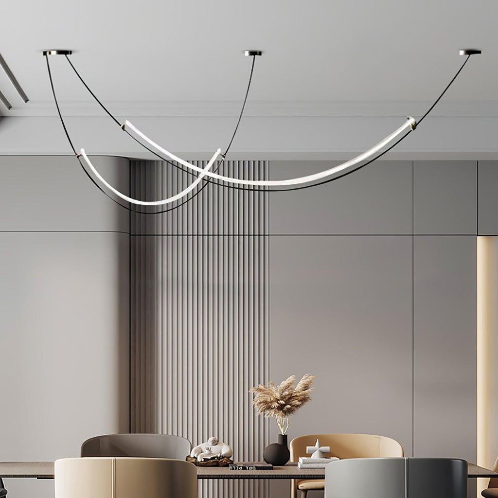 Two staggered curves of this Clérachic pendant glowing above a dining table, in front of grey fluted wall panelling.