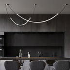 Clérachic pendant glowing over a dark kitchen with charcoal cabinets and a counter, grey stools in the foreground.