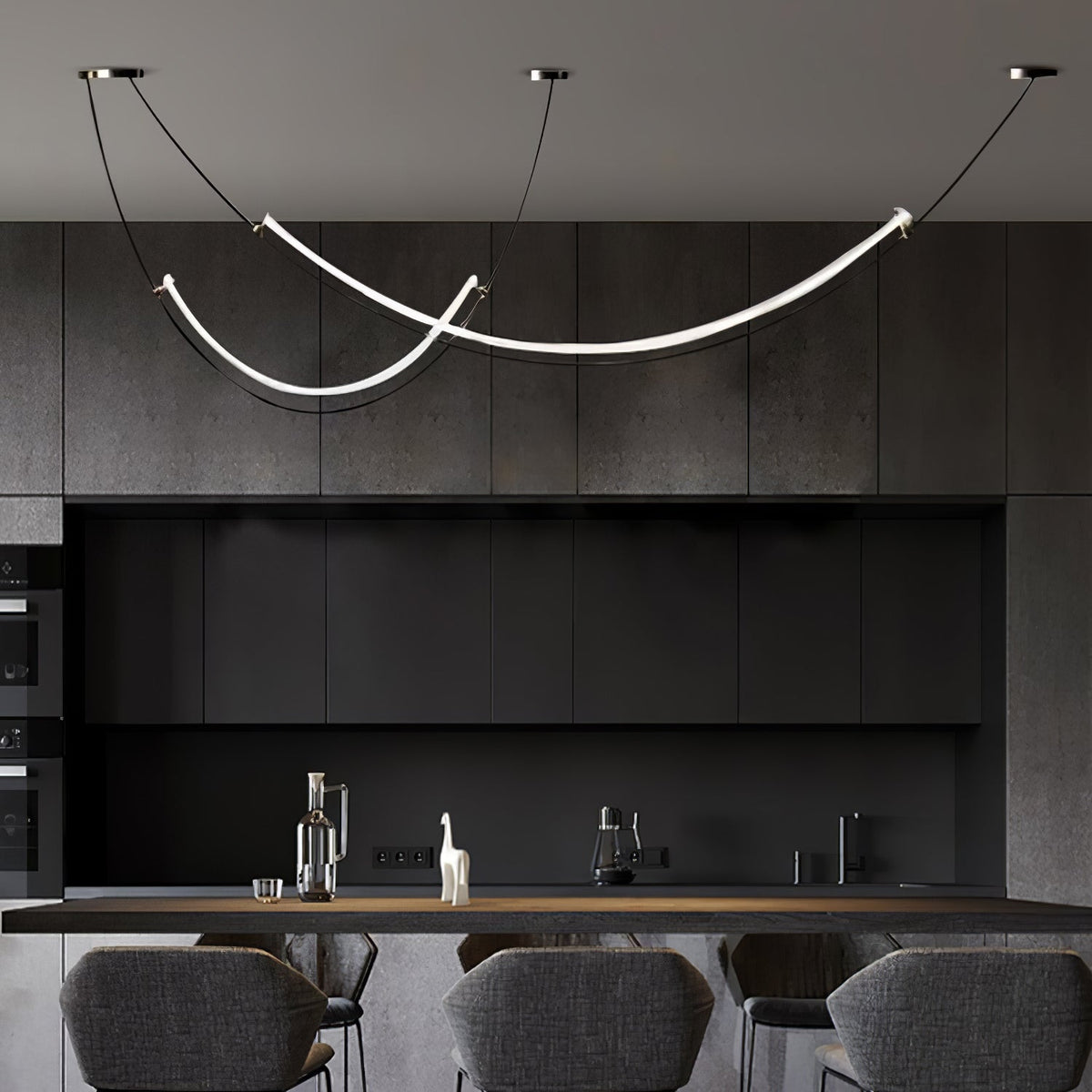 Clérachic pendant glowing over a dark kitchen with charcoal cabinets and a counter, grey stools in the foreground.