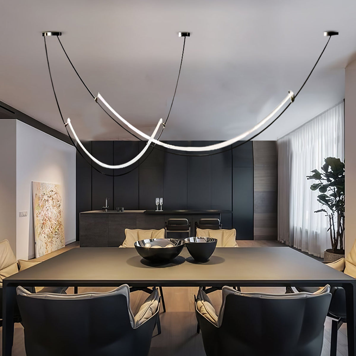 Clérachic pendant lit over a long black dining table with two dark bowls, grey armchairs and floor-length curtains behind.