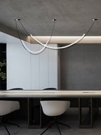 Lit Clérachic pendant above a long conference-style table with pale swivel chairs, under a ceiling with a soft cove light.