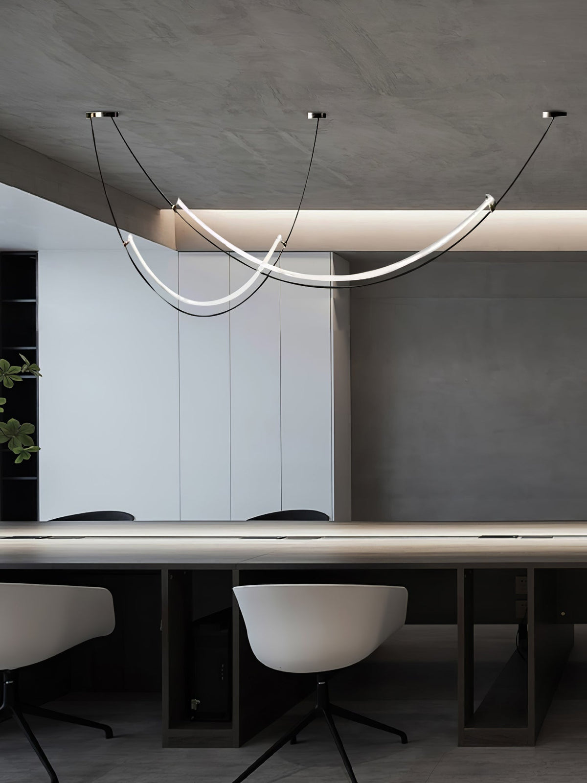Lit Clérachic pendant above a long conference-style table with pale swivel chairs, under a ceiling with a soft cove light.