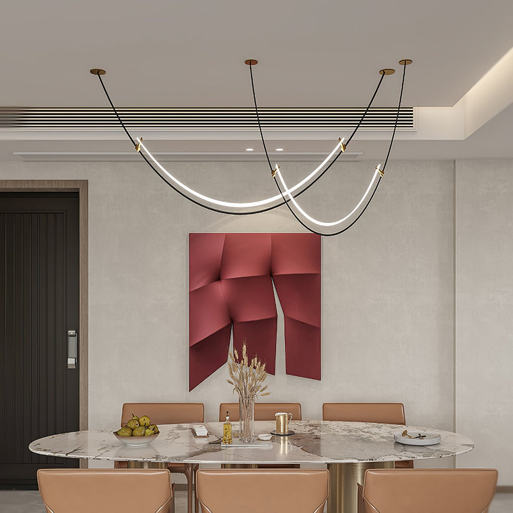 Clérachic pendant with gold canopies over a large oval marble table with tan chairs, a red sculptural panel on the wall behind.