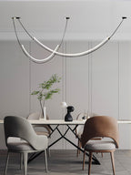 Clérachic pendant above a glass-and-black table with grey and brown chairs, a vase of branches beside a pale panelled wall.