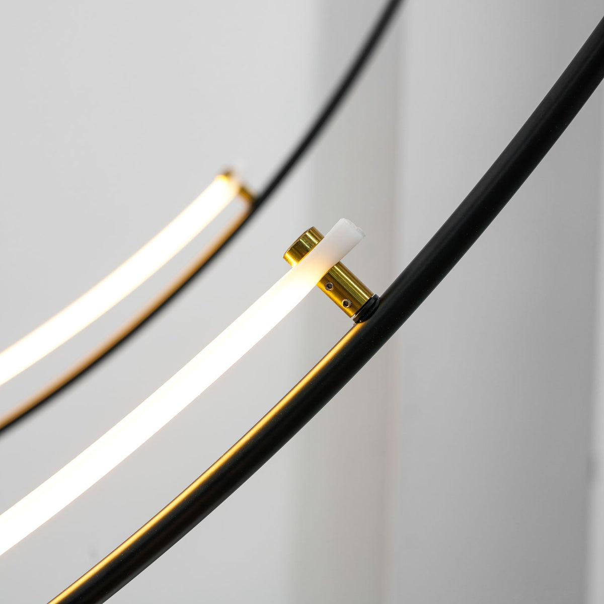 Close view of a gold collar joining the glowing LED bar to the black arm on this Clérachic pendant, with a second bar behind.
