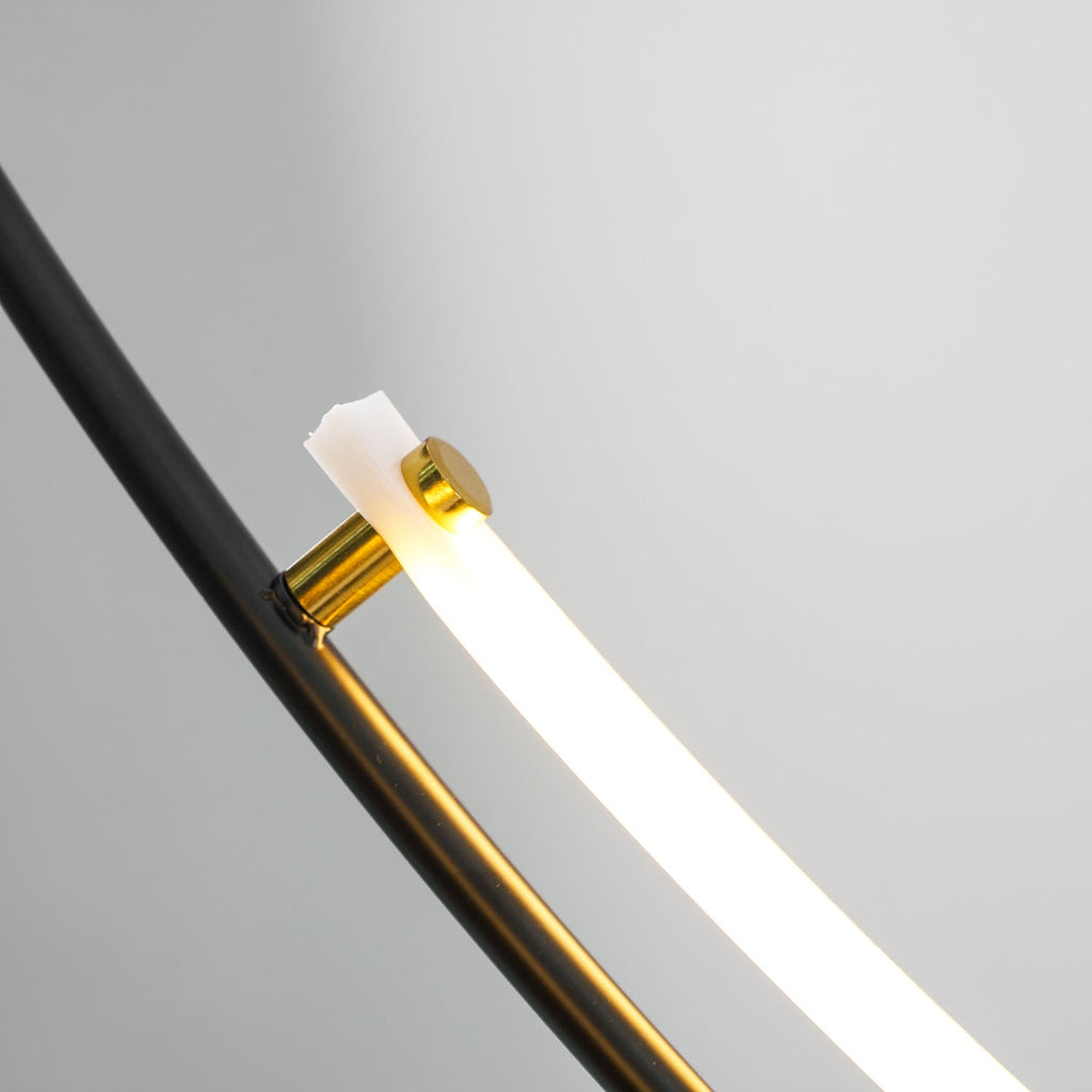 Close view of a brass-coloured fitting where the white LED bar meets the black arm of this Clérachic pendant, lit.