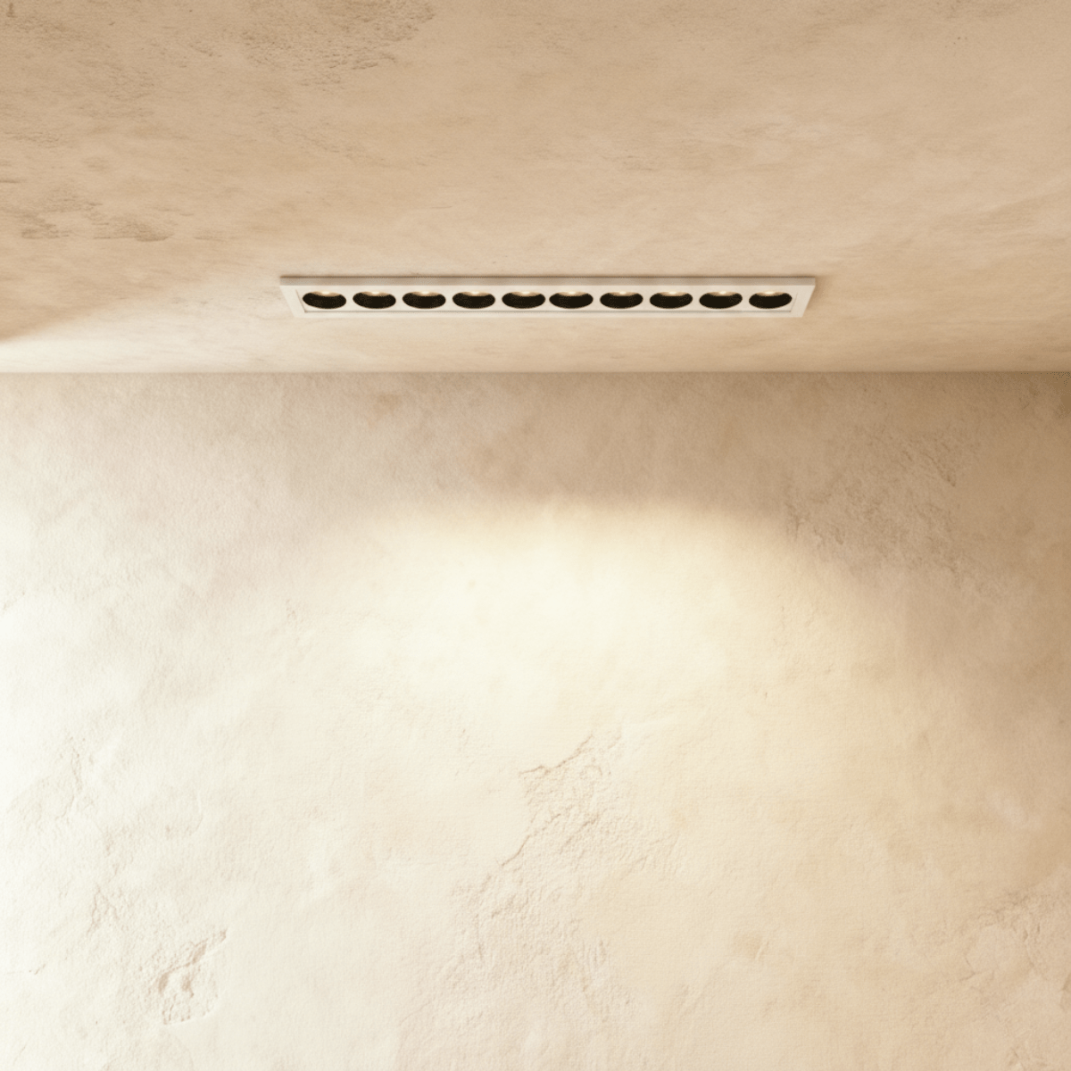 Clérachic recessed linear downlight in white with ten black reflectors, set flush in a limewashed ceiling and washing the wall below.