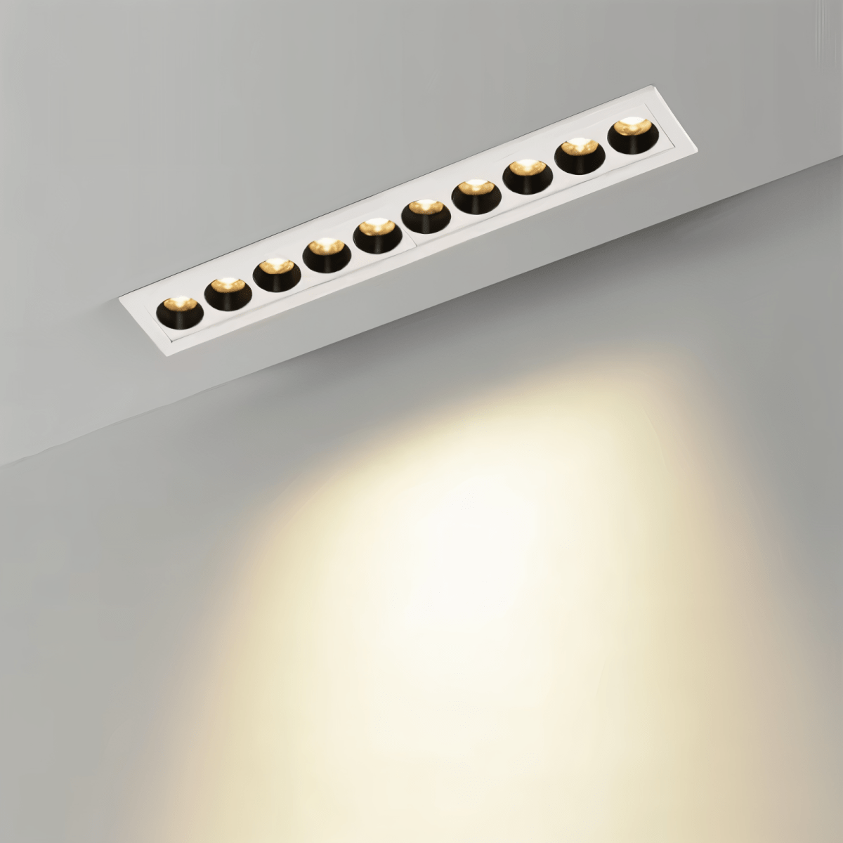 Clérachic slim white recessed downlight with ten deep-set black reflectors glowing warm white, throwing a soft pool of light on a grey wall.
