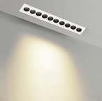 Clérachic recessed linear downlight in white with ten black round reflectors, seen from below with a warm wash of light on the wall.