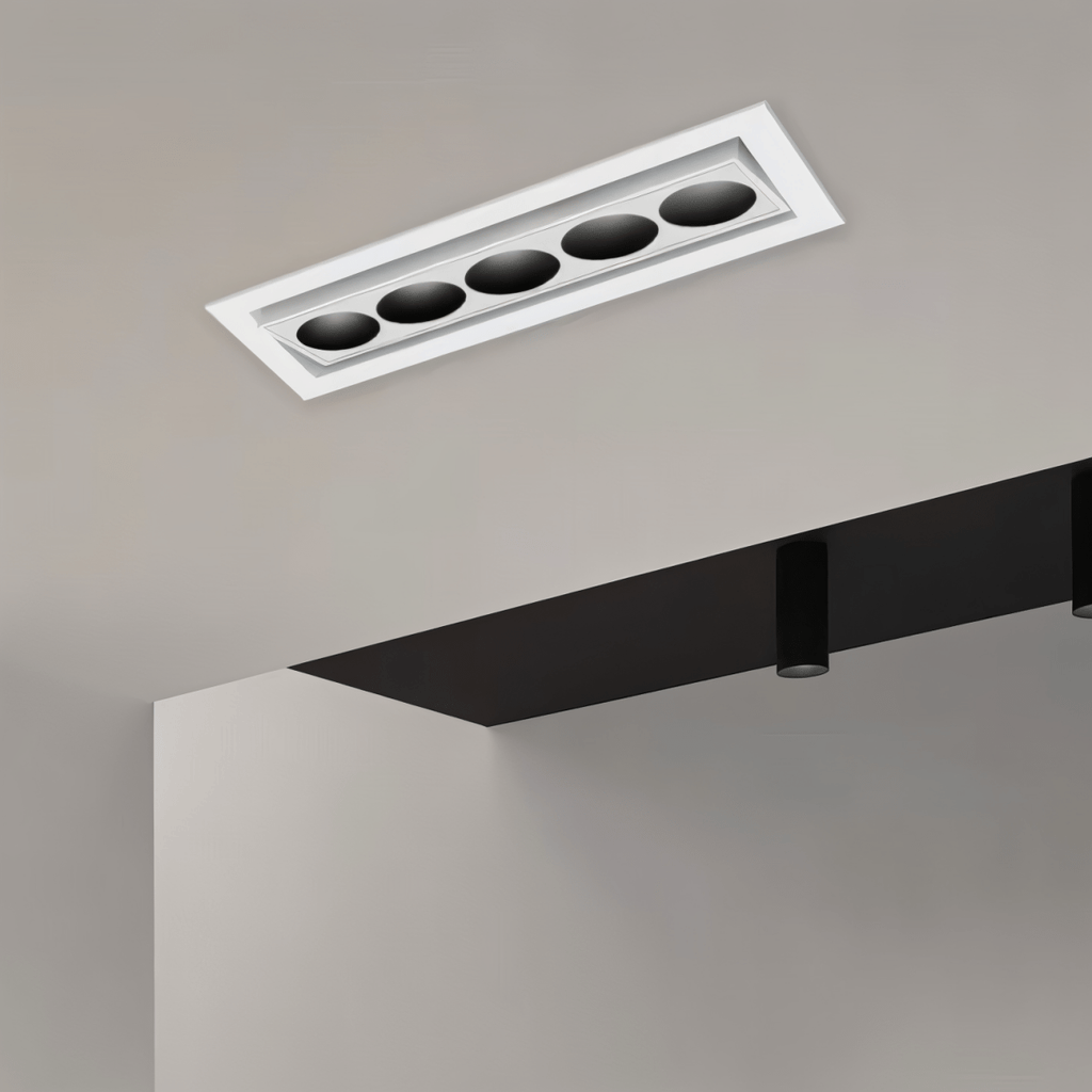 Clérachic white recessed downlight with five black reflectors on a tilting inner bar, fitted into a pale ceiling beside a dark bulkhead.