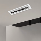Clérachic white recessed downlight with five black reflectors on a tilting inner bar, fitted into a pale ceiling beside a dark bulkhead.